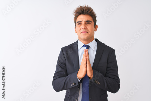 Young handsome businessman wearing suit standing over isolated white background begging and praying with hands together with hope expression on face very emotional and worried. Asking for forgiveness