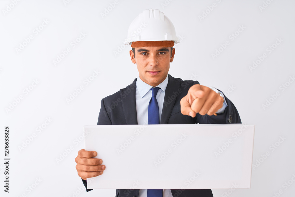 Young handsome architect man wearing helmet holding banner over isolated white background pointing with finger to the camera and to you, hand sign, positive and confident gesture from the front Young handsome architect man wearing helmet holding banner over isolated white background pointing with finger to the camera and to you, hand sign, positive and confident gesture from the front