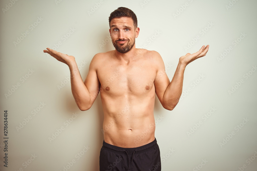 Young handsome shirtless man over isolated background clueless and confused expression with arms and hands raised. Doubt concept.