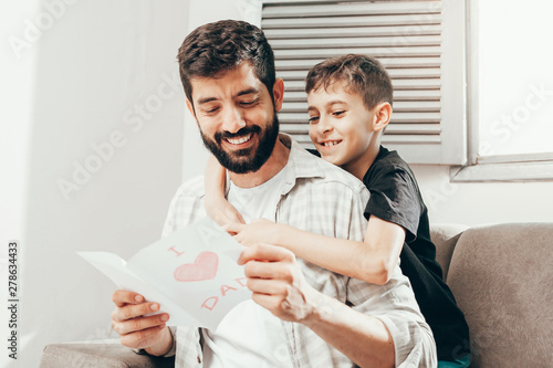 Happy father's day! Son congratulating dad and giving him a greeting card. Daddy and son smiling and hugging. Family holiday and togetherness.