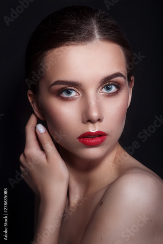 Portrait of beautiful young woman with perfect young skin and red lips on dark background