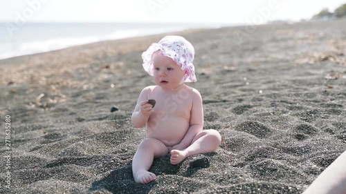 A yearling naked girl plays with stones on the sea beach