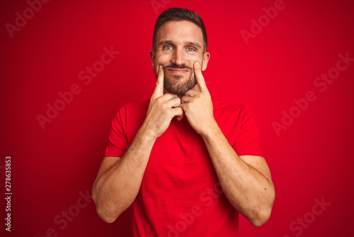 Young handsome man wearing casual t-shirt over red isolated background Smiling with open mouth, fingers pointing and forcing cheerful smile