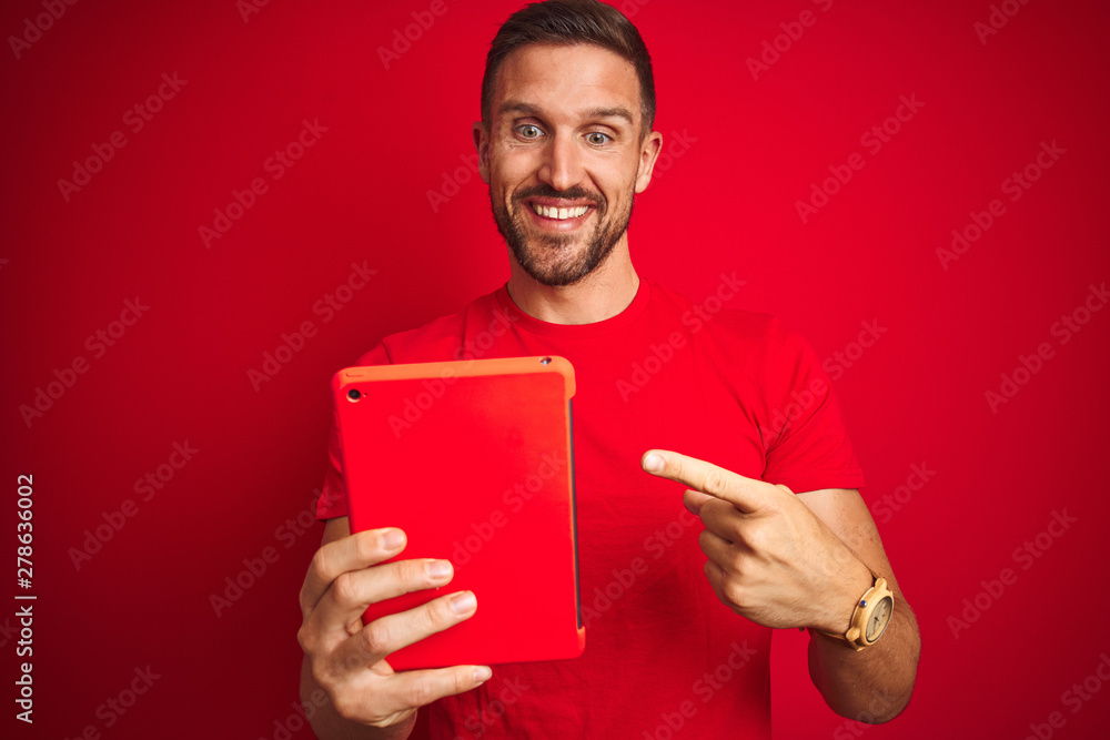 Young man using digital touchpad tablet over red isolated background very happy pointing with hand and finger Young man using digital touchpad tablet over red isolated background very happy pointing with hand and finger