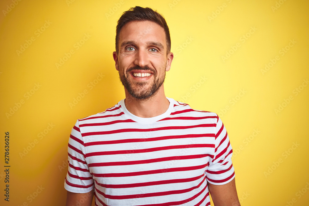 Young handsome man wearing casual red striped t-shirt over yellow isolated background with a happy and cool smile on face. Lucky person. Young handsome man wearing casual red striped t-shirt over yellow isolated background with a happy and cool smile on face. Lucky person.