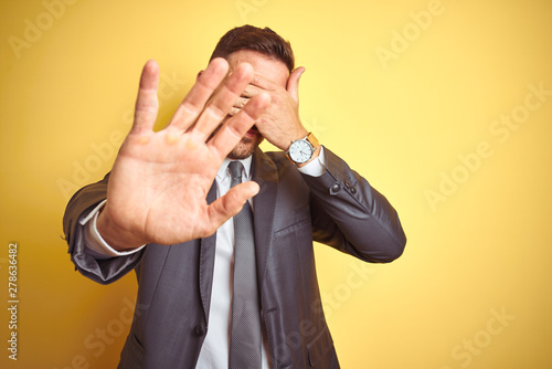 Young handsome business man over yellow isolated background covering eyes with hands and doing stop gesture with sad and fear expression. Embarrassed and negative concept.