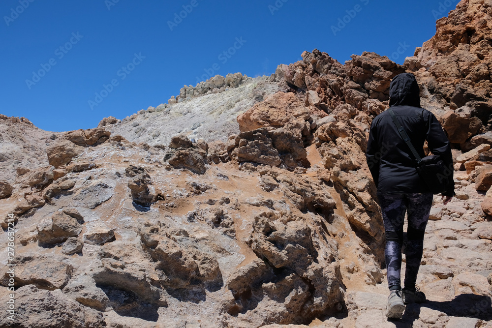 Woman ascending the Teide mountain peak on a dry and rocky volcanic landscape