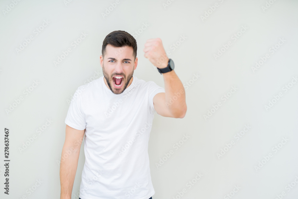 Young handsome man wearing casual white t-shirt over isolated background angry and mad raising fist frustrated and furious while shouting with anger. Rage and aggressive concept. Young handsome man wearing casual white t-shirt over isolated background angry and mad raising fist frustrated and furious while shouting with anger. Rage and aggressive concept.