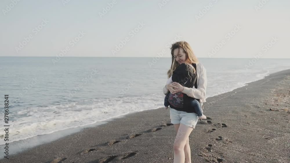 A mother holds her baby in a sling and walks along the sea coast A mother holds her baby in a sling and walks along the sea coast