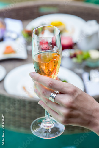 Close up image of a woman holding a glass of champagne, a meal next to the pool, leisure vacation travel summertime concept