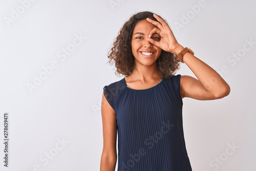 Young brazilian woman wearing blue dress standing over isolated white background doing ok gesture with hand smiling  eye looking through fingers with happy face.