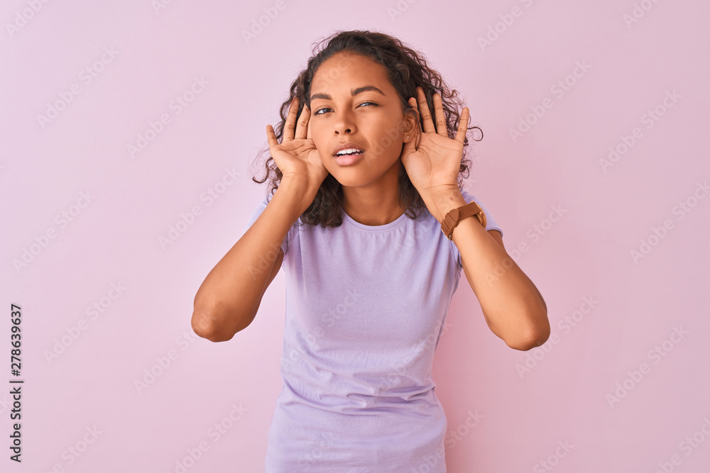 Young brazilian woman wearing t-shirt standing over isolated pink background Trying to hear both hands on ear gesture, curious for gossip. Hearing problem, deaf Young brazilian woman wearing t-shirt standing over isolated pink background Trying to hear both hands on ear gesture, curious for gossip. Hearing problem, deaf