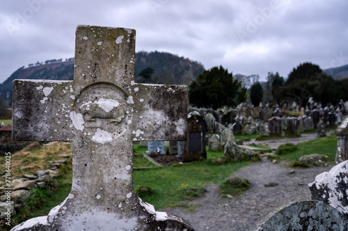 Old catholic granite cross on tombstone with cemetery and tombstones in background, Glendalough, Ireland