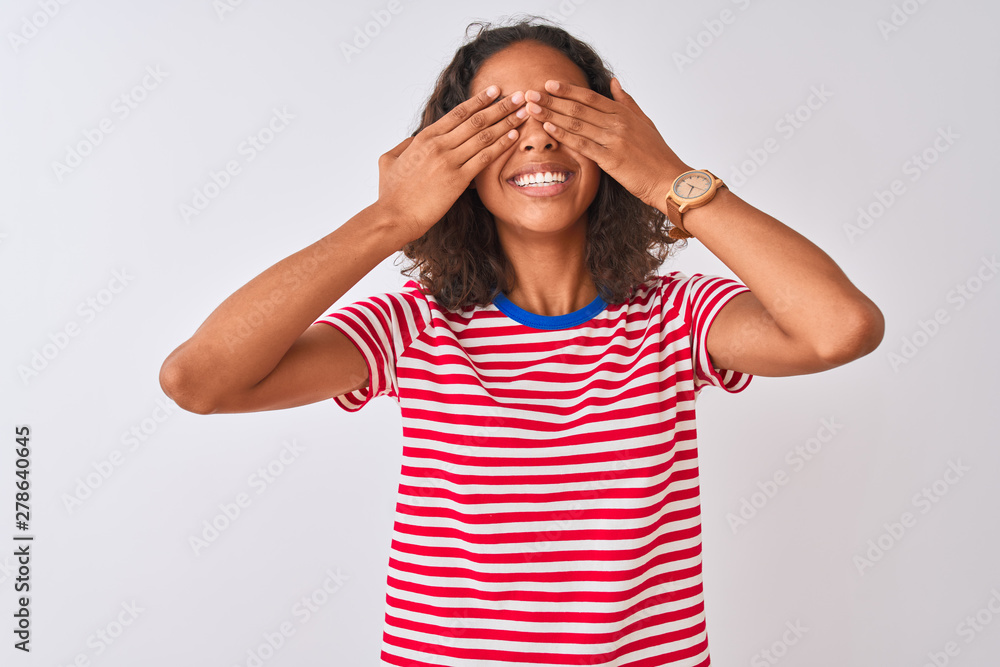Young brazilian woman wearing red striped t-shirt standing over isolated white background covering eyes with hands smiling cheerful and funny. Blind concept. Young brazilian woman wearing red striped t-shirt standing over isolated white background covering eyes with hands smiling cheerful and funny. Blind concept.