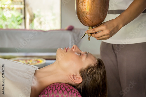 Shirodhara, an Ayurvedic healing technique. Oil dripping on the female forehead. Portrait of a young woman at an ayurvedic massage session with aromatic oil dripping on her forehead and hair. photo