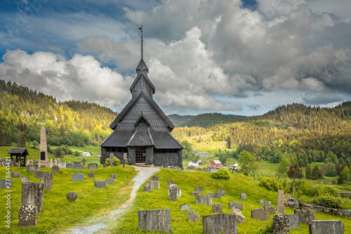 Eidsborg medieval wooden Stave Church and graveyard in front with green forest and cloud sky in the backround, Tokke, Telemark county, Norway photo