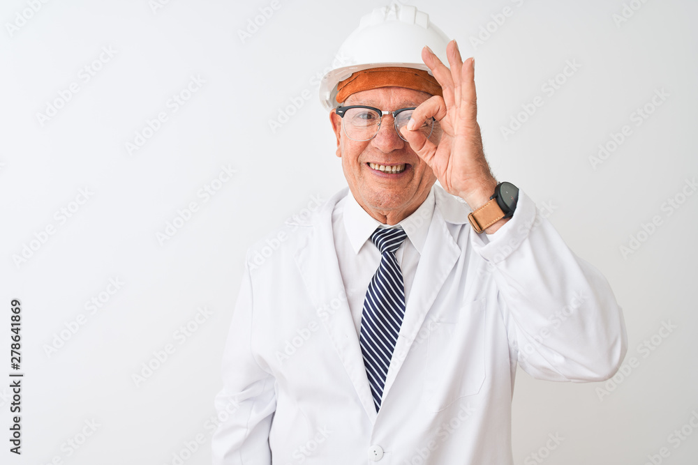 Senior grey-haired engineer man wearing coat and helmet over isolated white background doing ok gesture with hand smiling, eye looking through fingers with happy face. Senior grey-haired engineer man wearing coat and helmet over isolated white background doing ok gesture with hand smiling, eye looking through fingers with happy face.