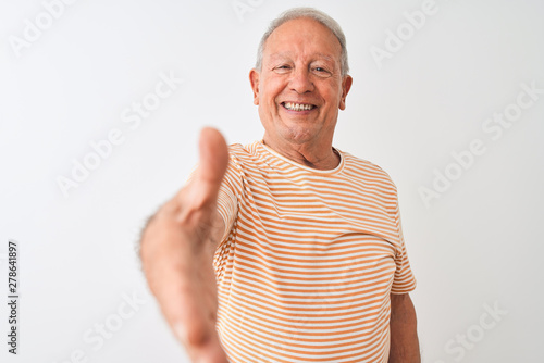 Senior grey-haired man wearing striped t-shirt standing over isolated white background smiling friendly offering handshake as greeting and welcoming. Successful business.