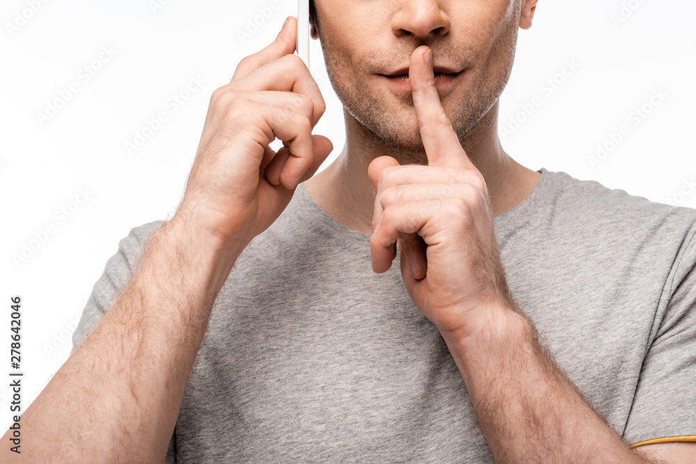 Fototapeta premium cropped view of man showing silence gesture while using smartphone isolated on white