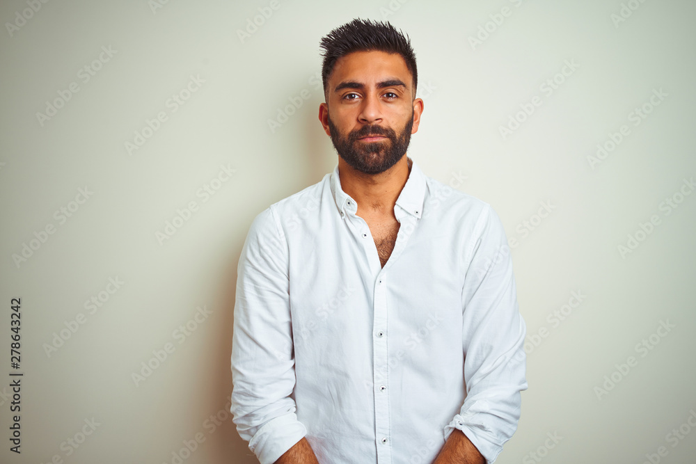 Young indian man wearing elegant shirt standing over isolated white  background with serious expression on face. Simple and natural looking at  the camera. foto de Stock | Adobe Stock