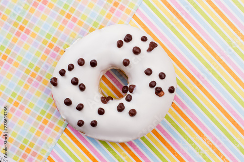 Donut on colored paper background. White glazed donut with chocolate crunchies. Freshly baked snack.