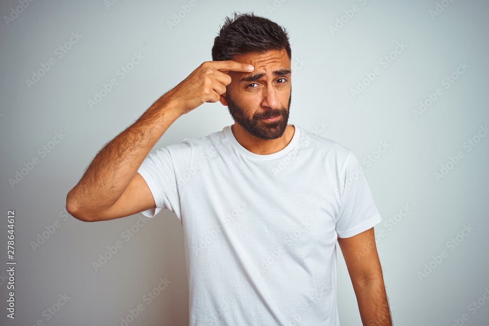Young indian man wearing t-shirt standing over isolated white background pointing unhappy to pimple on forehead, ugly infection of blackhead. Acne and skin problem Young indian man wearing t-shirt standing over isolated white background pointing unhappy to pimple on forehead, ugly infection of blackhead. Acne and skin problem