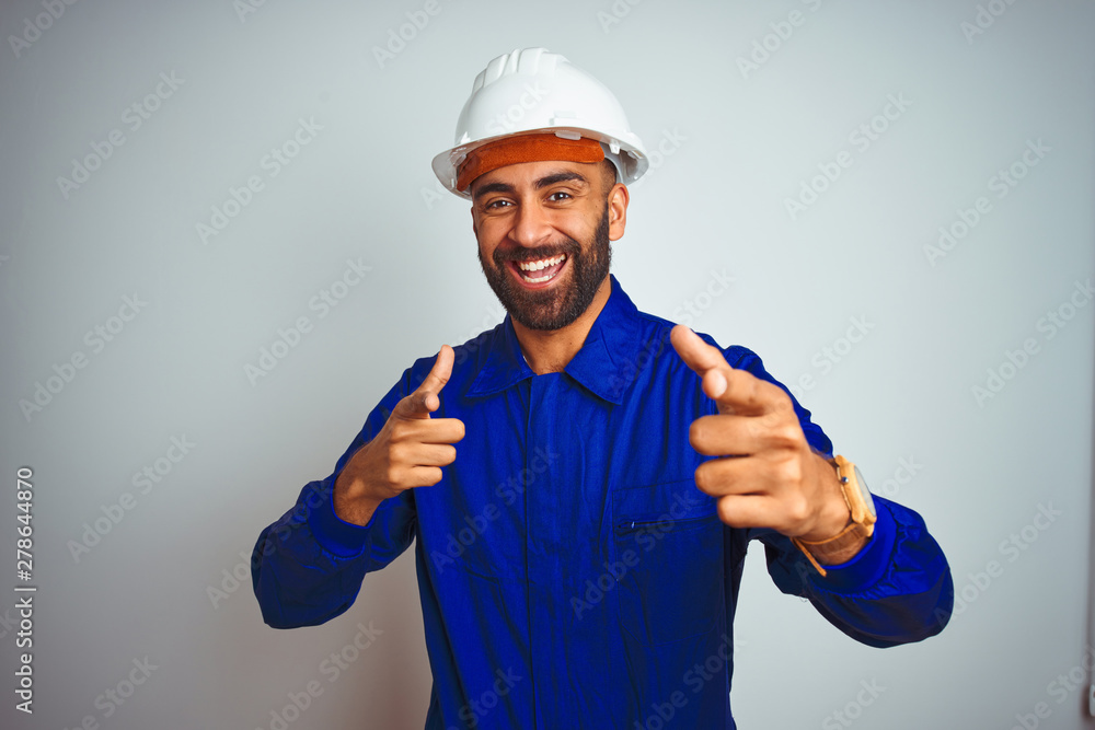 Handsome indian worker man wearing uniform and helmet over isolated white background pointing fingers to camera with happy and funny face. Good energy and vibes.