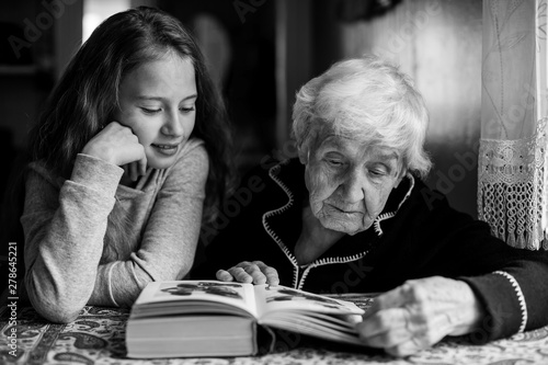 An old woman - a granny with a little girl - granddaughter reading a book. Black and white photography.
