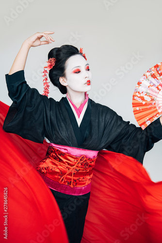 geisha in black kimono with hand fan and red cloth on background dancing isolated on white