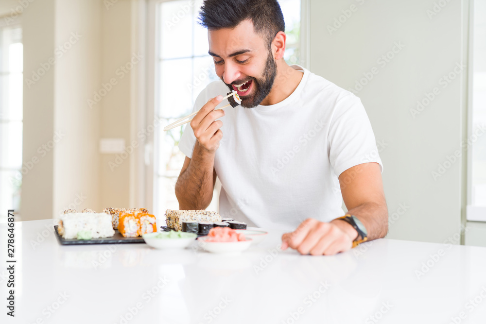 Handsome man smiling happy enjoying eating fresh colorful asian sushi using chopsticks Handsome man smiling happy enjoying eating fresh colorful asian sushi using chopsticks