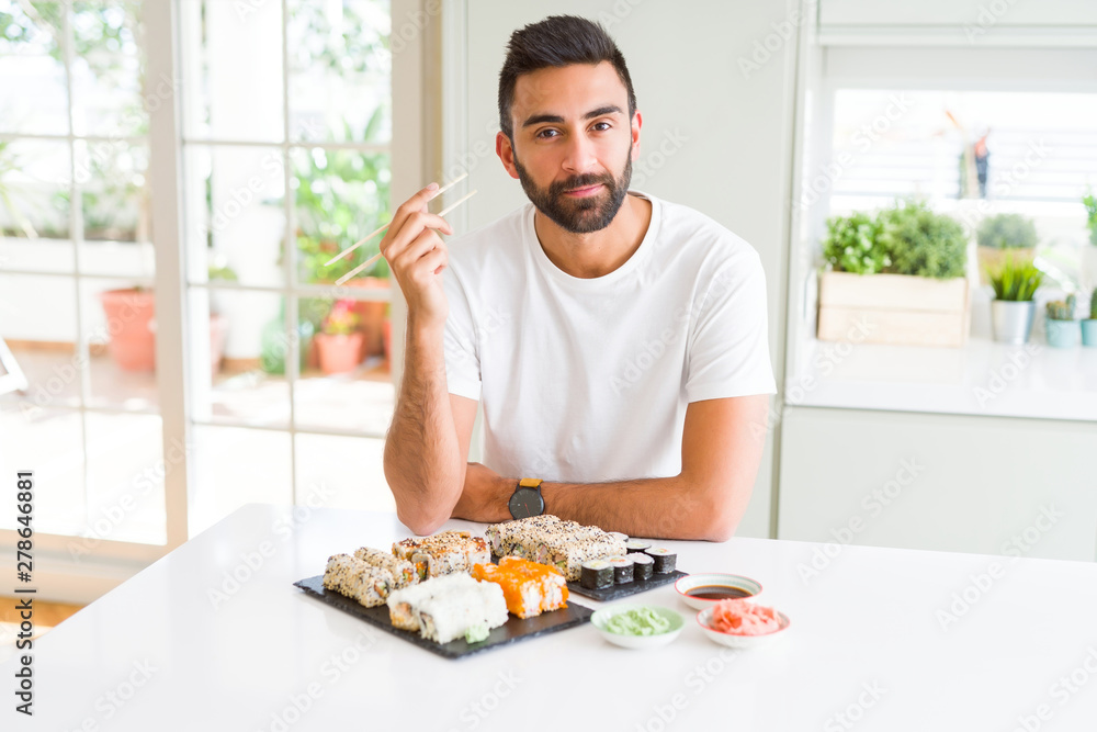 Handsome hispanic man eating asian sushi using chopsticks with a confident expression on smart face thinking serious Handsome hispanic man eating asian sushi using chopsticks with a confident expression on smart face thinking serious