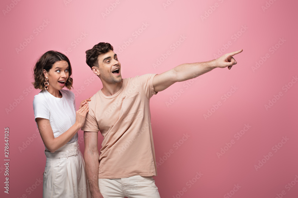 excited man pointing with finger near surprised woman on pink background excited man pointing with finger near surprised woman on pink background
