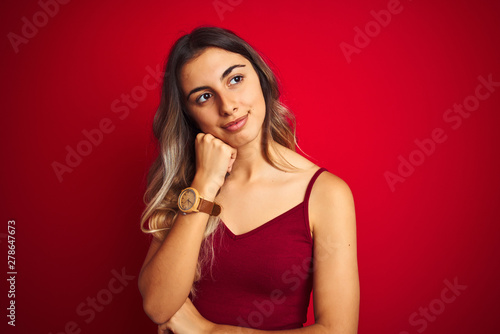 Young beautiful woman wearing a t-shirt over red isolated background with hand on chin thinking about question, pensive expression. Smiling with thoughtful face. Doubt concept.