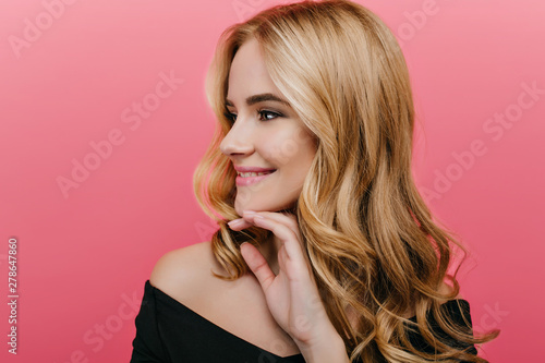 Close-up portrait of gorgeous young woman with shiny hair isolated on pink background. Indoor photo of fair-haired ecstatic girl looking away with gently smile.