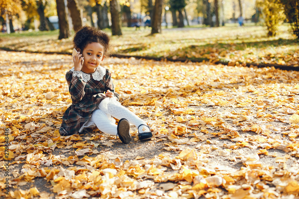 little beautiful dark-skinned girl walks in the autumn park with phone little beautiful dark-skinned girl walks in the autumn park with phone