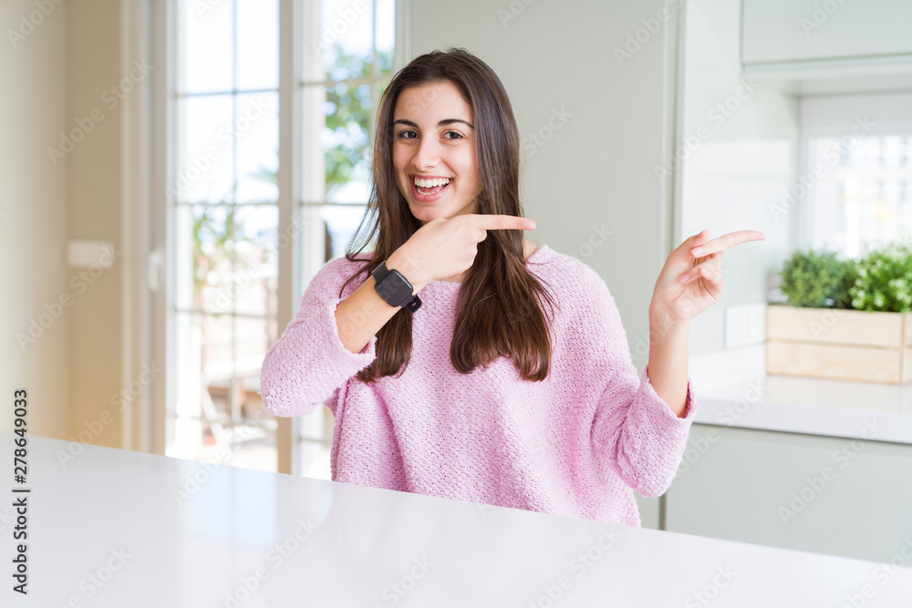 Beautiful young woman wearing pink sweater smiling and looking at the camera pointing with two hands and fingers to the side.