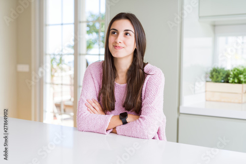 Beautiful young woman wearing pink sweater smiling looking side and staring away thinking.