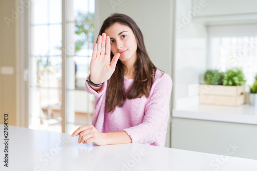 Beautiful young woman wearing pink sweater doing stop sing with palm of the hand. Warning expression with negative and serious gesture on the face.
