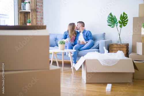 Young couple relaxing drinking a cup of coffee sitting at sofa of  new home with cardboard boxes around them, very happy moving to a new apartment
