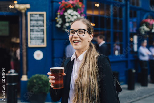 Young business lady in glasses standing by the pub with a pint of the beer.