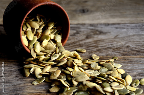 Peeled pumpkin seeds are scattered from wooden dishes on a wooden table ..