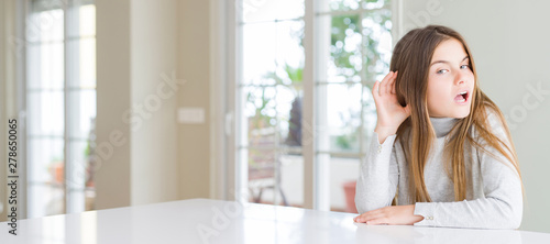 Wide angle picture of beautiful young girl kid wearing casual sweater smiling with hand over ear listening an hearing to rumor or gossip. Deafness concept.