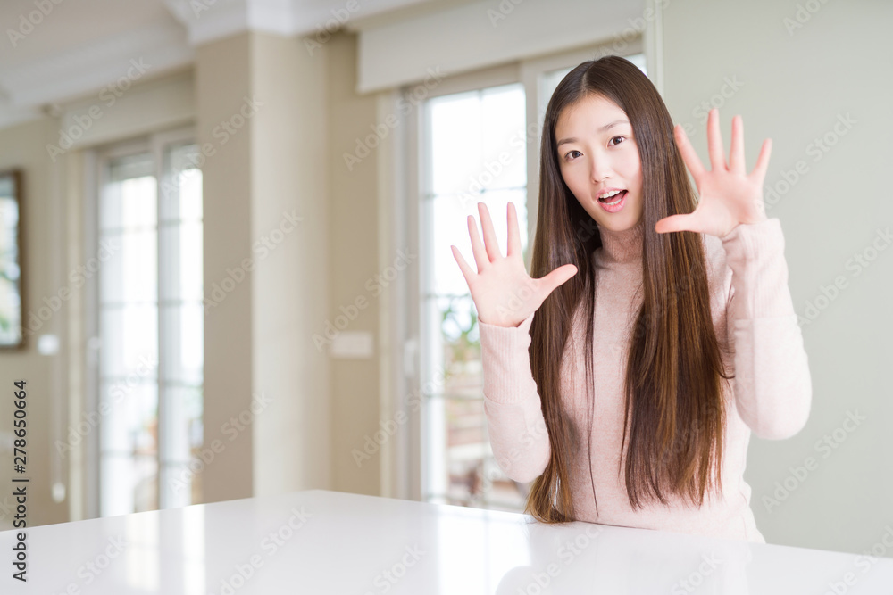 Beautiful Asian woman wearing casual sweater on white table afraid and terrified with fear expression stop gesture with hands, shouting in shock. Panic concept. Beautiful Asian woman wearing casual sweater on white table afraid and terrified with fear expression stop gesture with hands, shouting in shock. Panic concept.