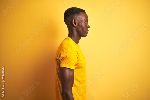 Young african american man wearing casual t-shirt standing over isolated yellow background looking to side, relax profile pose with natural face and confident smile.