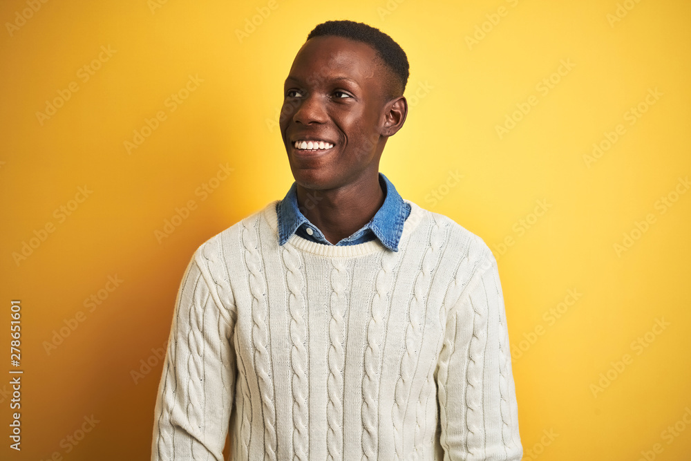 African american man wearing denim shirt and white sweater over isolated yellow background looking away to side with smile on face, natural expression. Laughing confident. African american man wearing denim shirt and white sweater over isolated yellow background looking away to side with smile on face, natural expression. Laughing confident.