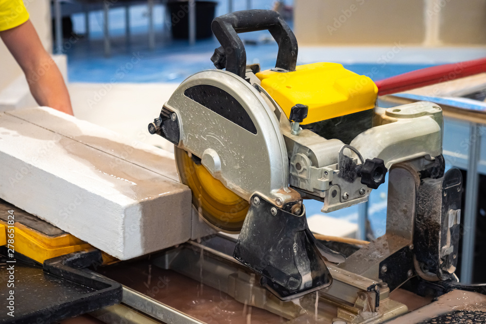 Worker sawing stone slab. Circular saw. Stone and tile cutting equipment.  The shop is equipped with a circular saw. Ceramic tile and stone cutting  machine. Processing of stone and tile. Stock Photo
