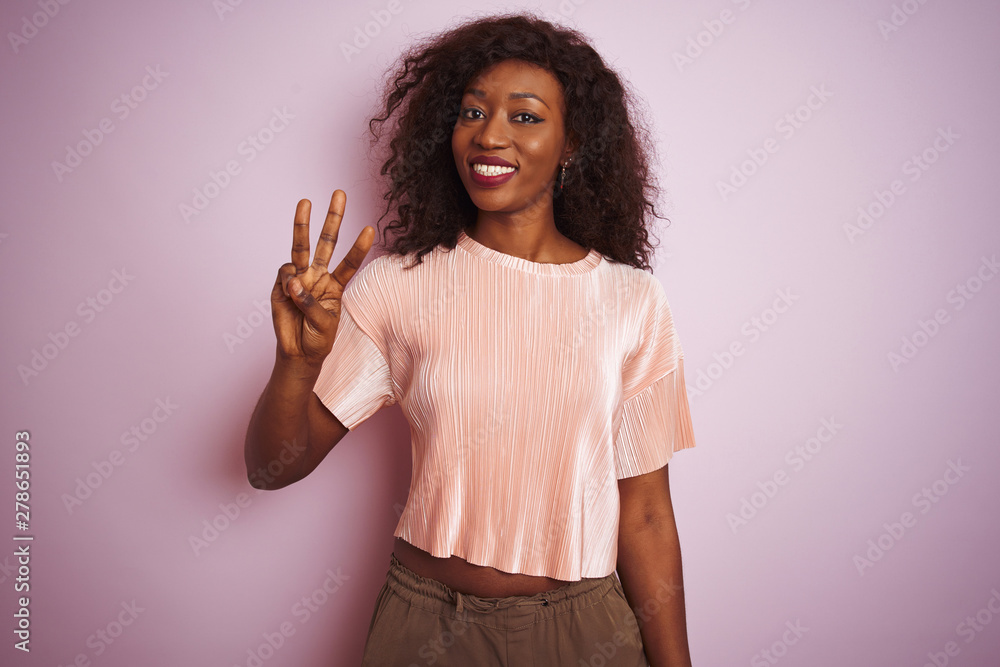 Young african american woman wearing t-shirt standing over isolated pink background showing and pointing up with fingers number three while smiling confident and happy. Young african american woman wearing t-shirt standing over isolated pink background showing and pointing up with fingers number three while smiling confident and happy.