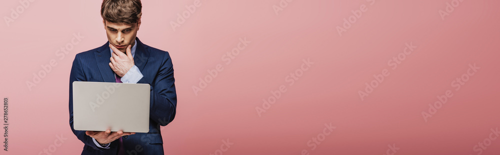 panoramic shot of thoughtful businessman using laptop on pink background panoramic shot of thoughtful businessman using laptop on pink background