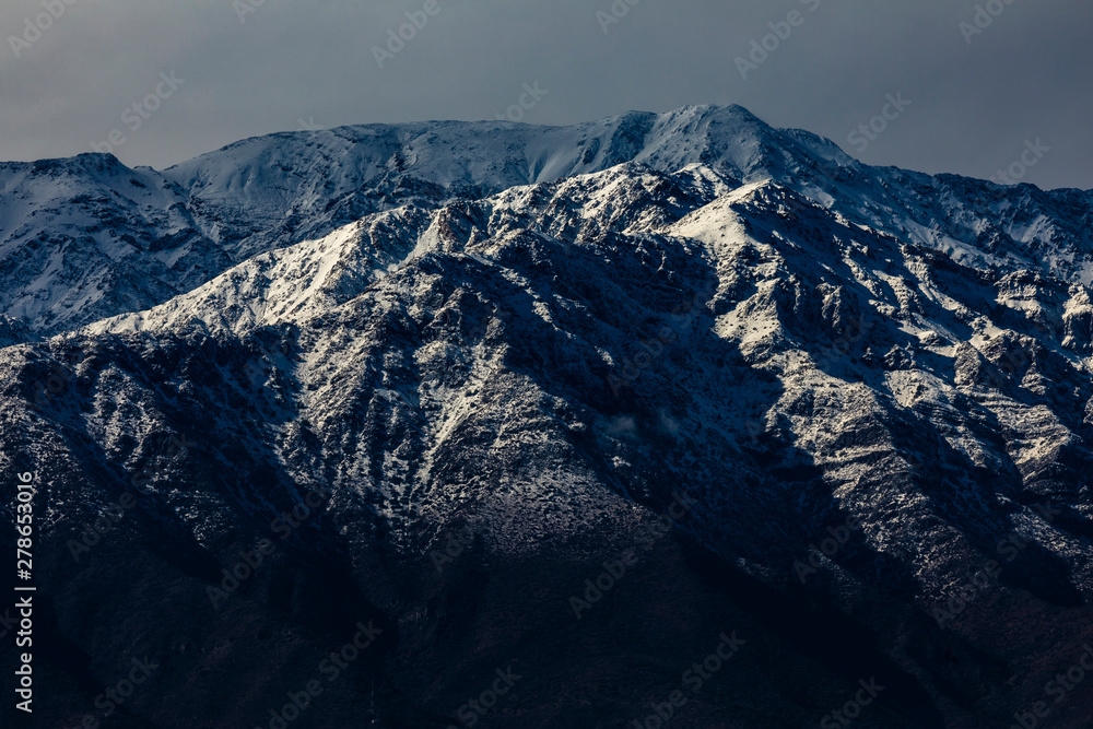 Fototapeta premium Cerro Ramon and Cerro La Cruz summits during a winter day. Snowcapped summits at central Andes mountains and amazing snowy rugged landscape on a cloudy day, an awe outdoor winter background scenery