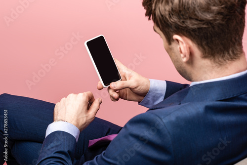 cropped view of businessman sitting and holding smartphone with blank screen isolated on pink